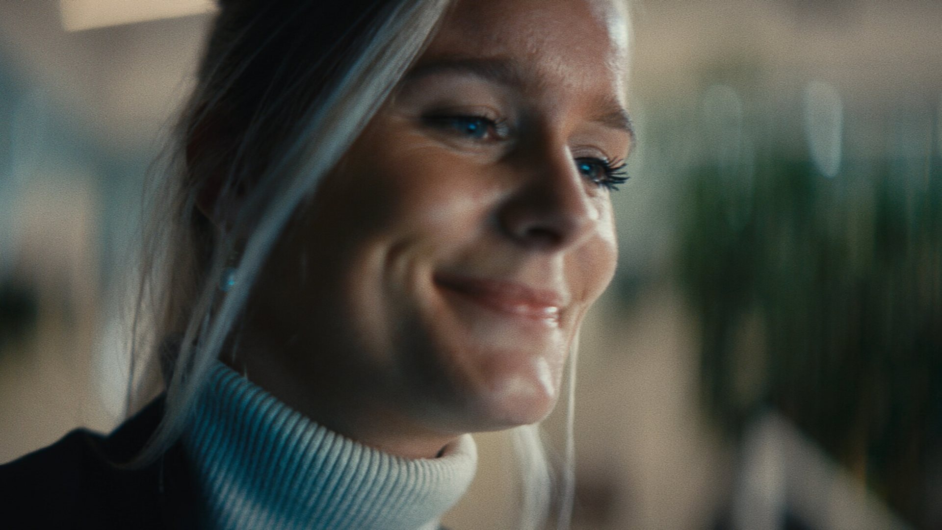 A woman with blonde hair smiles while looking away from the camera.