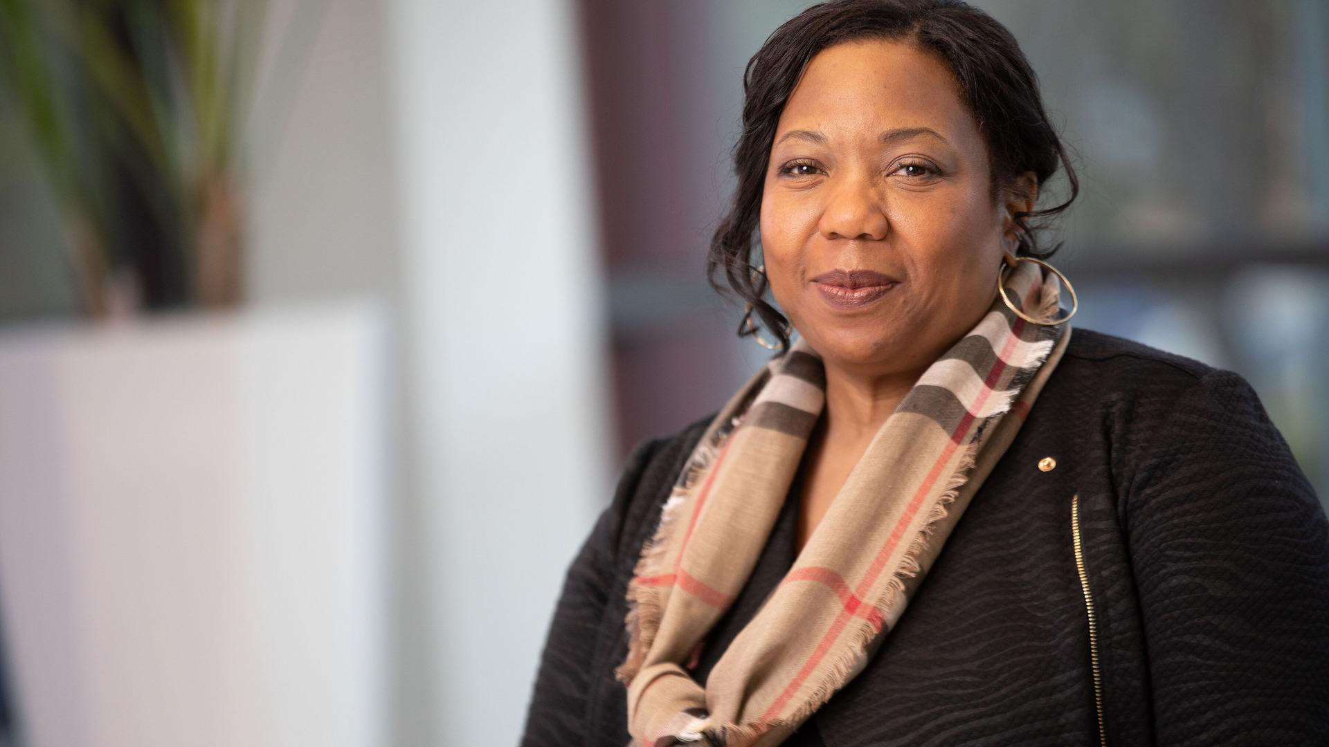 A woman in a black sweater and striped scarf smiles at the camera.