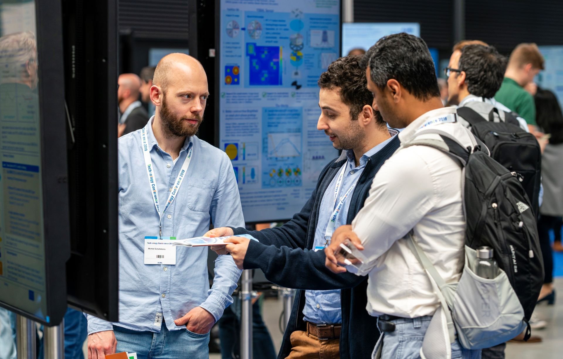 Two men ask another man a question while standing in front of a project poster at the ASML Technology Conference. Two men ask another man a question while standing in front of a project poster at the ASML Technology Conference.