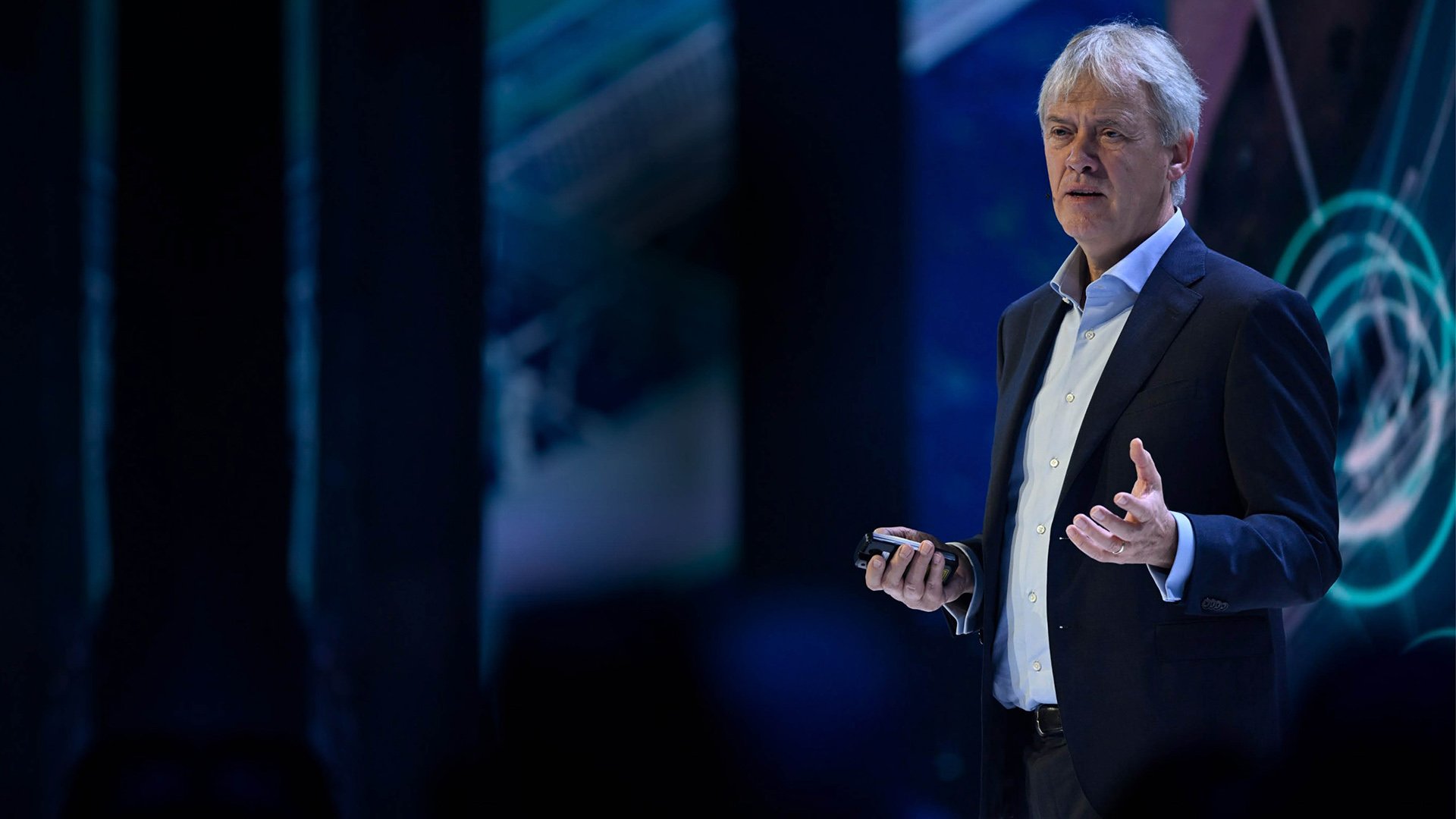 A picture of Peter Wennink giving a speech on stage, holding a remote control in one hand. A picture of Peter Wennink giving a speech on stage, holding a remote control in one hand.