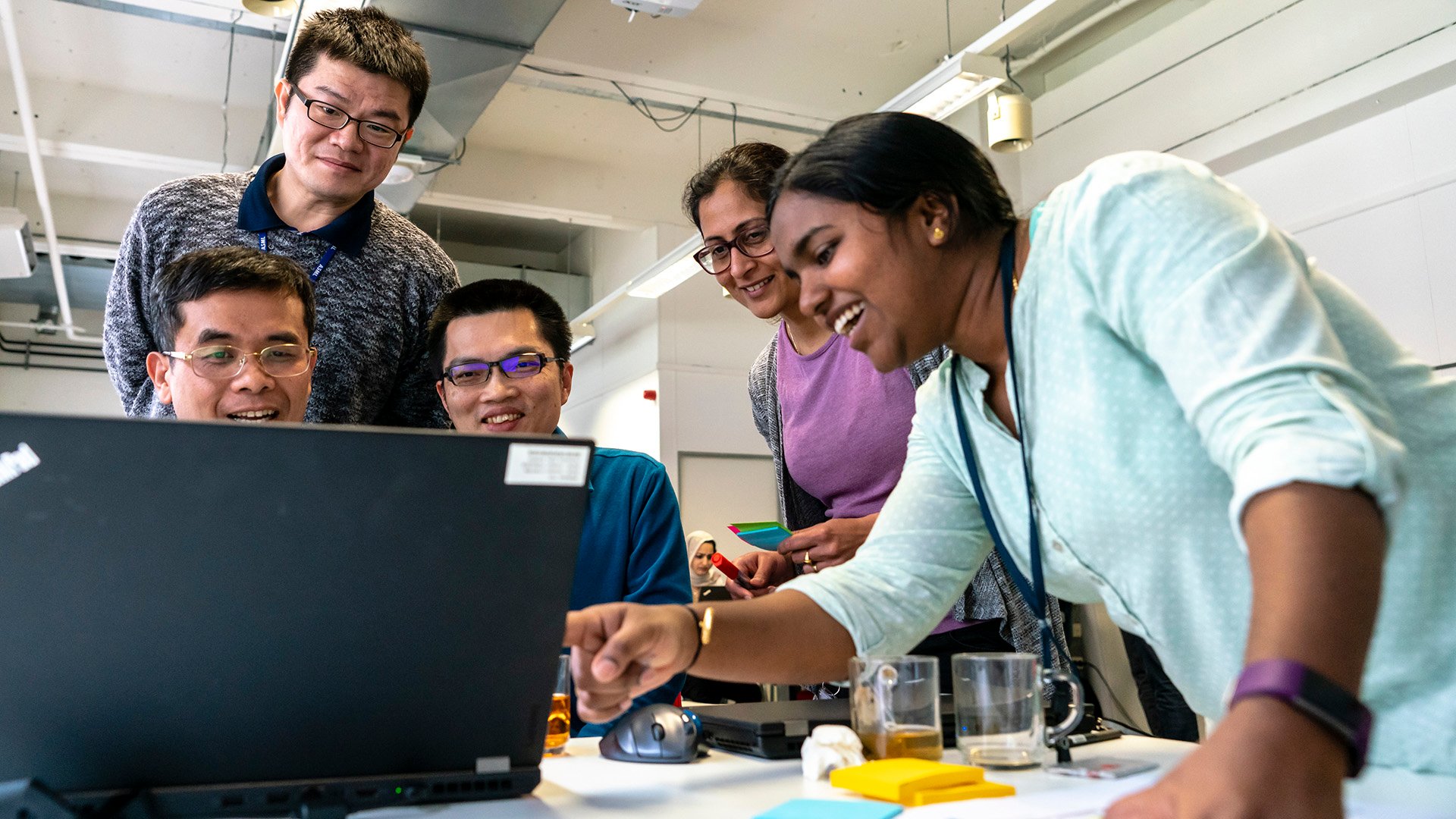A young woman points to a laptop screen as other colleagues gather round a table at an ASML Agile event.