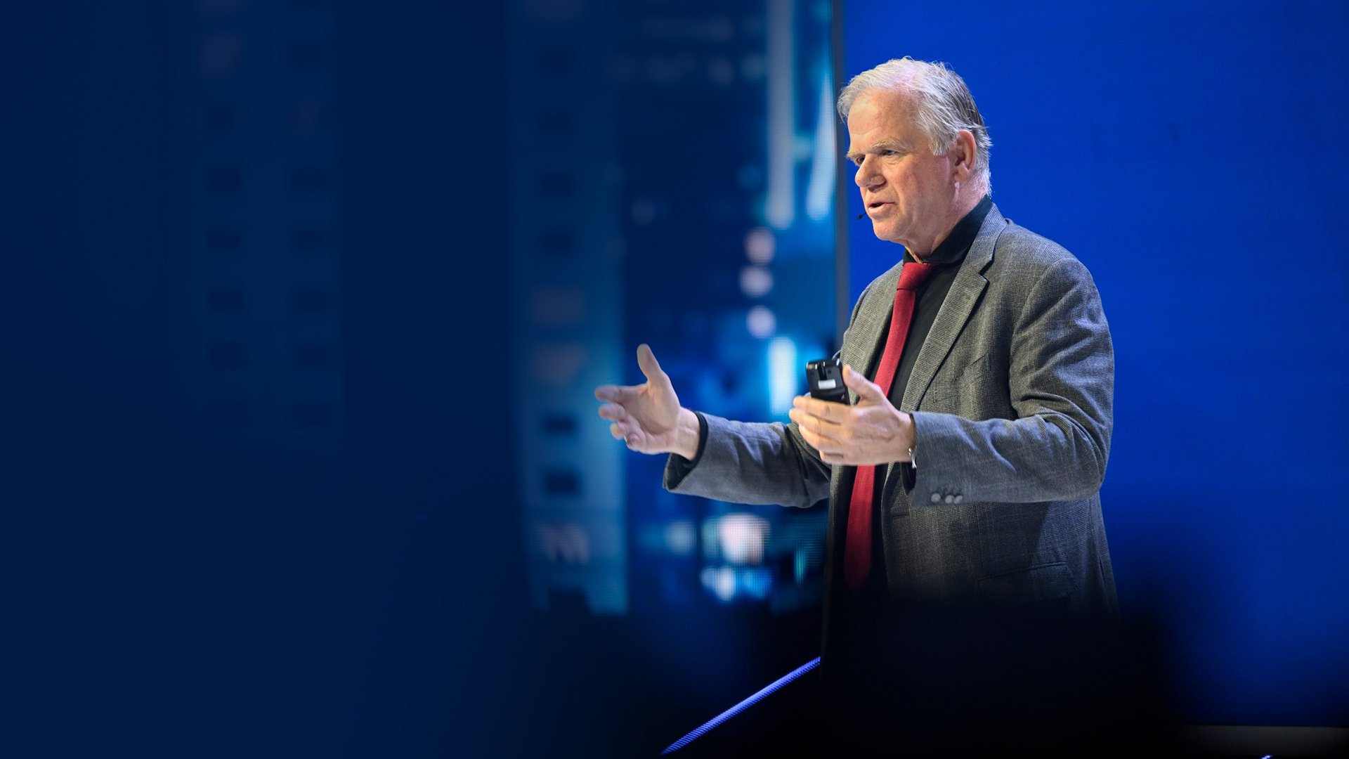 Martin van der Brink giving a presentation with a remote in hand, dressed in a grey jacket and red tie. Martin van der Brink giving a presentation with a remote in hand, dressed in a grey jacket and red tie.