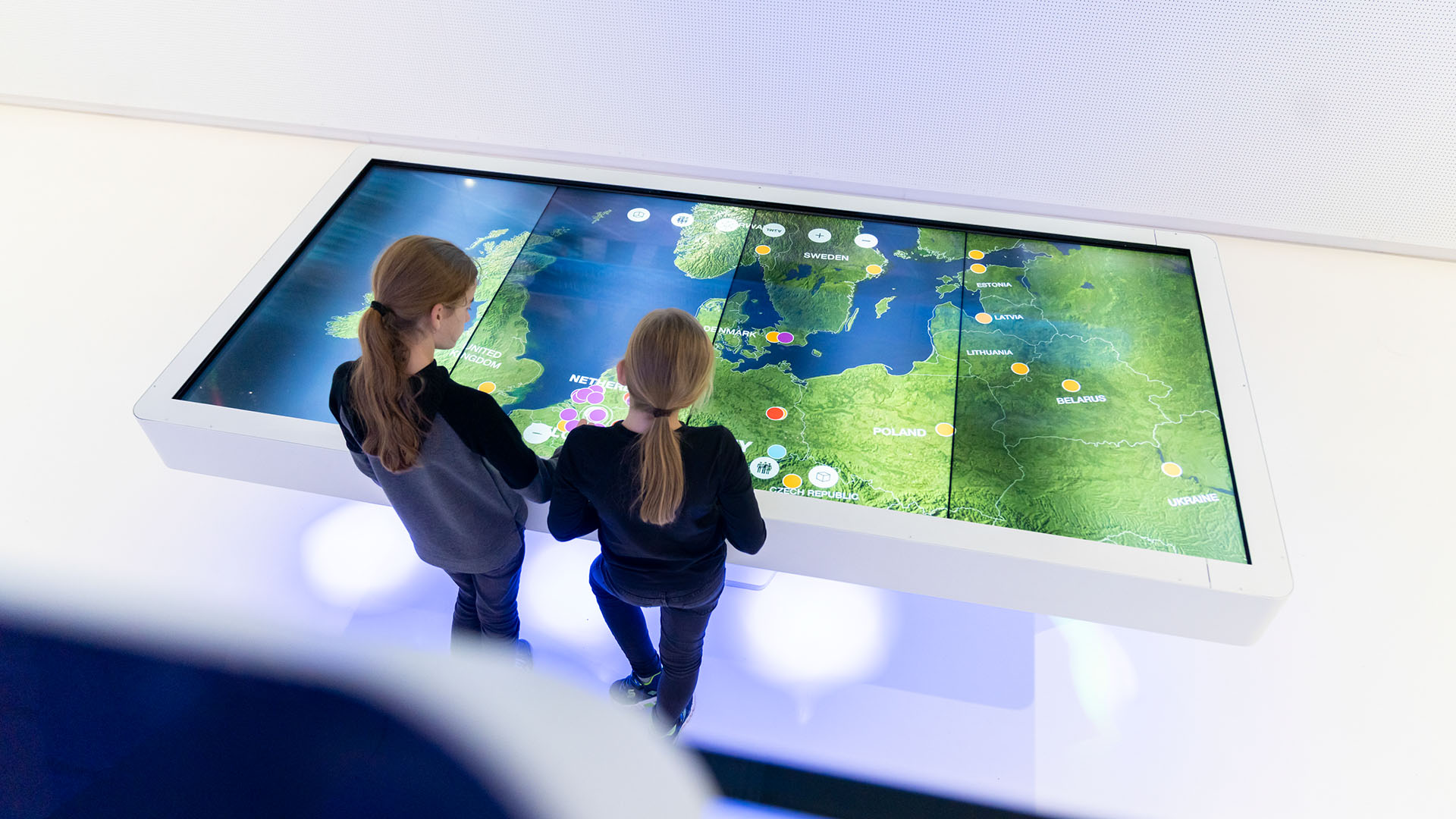 Two people interacting with a large, interactive digital map display at ASML's Experience Center, engaging with geographical information showing various locations and data points. Two people interacting with a large, interactive digital map display at ASML's Experience Center, engaging with geographical information showing various locations and data points.