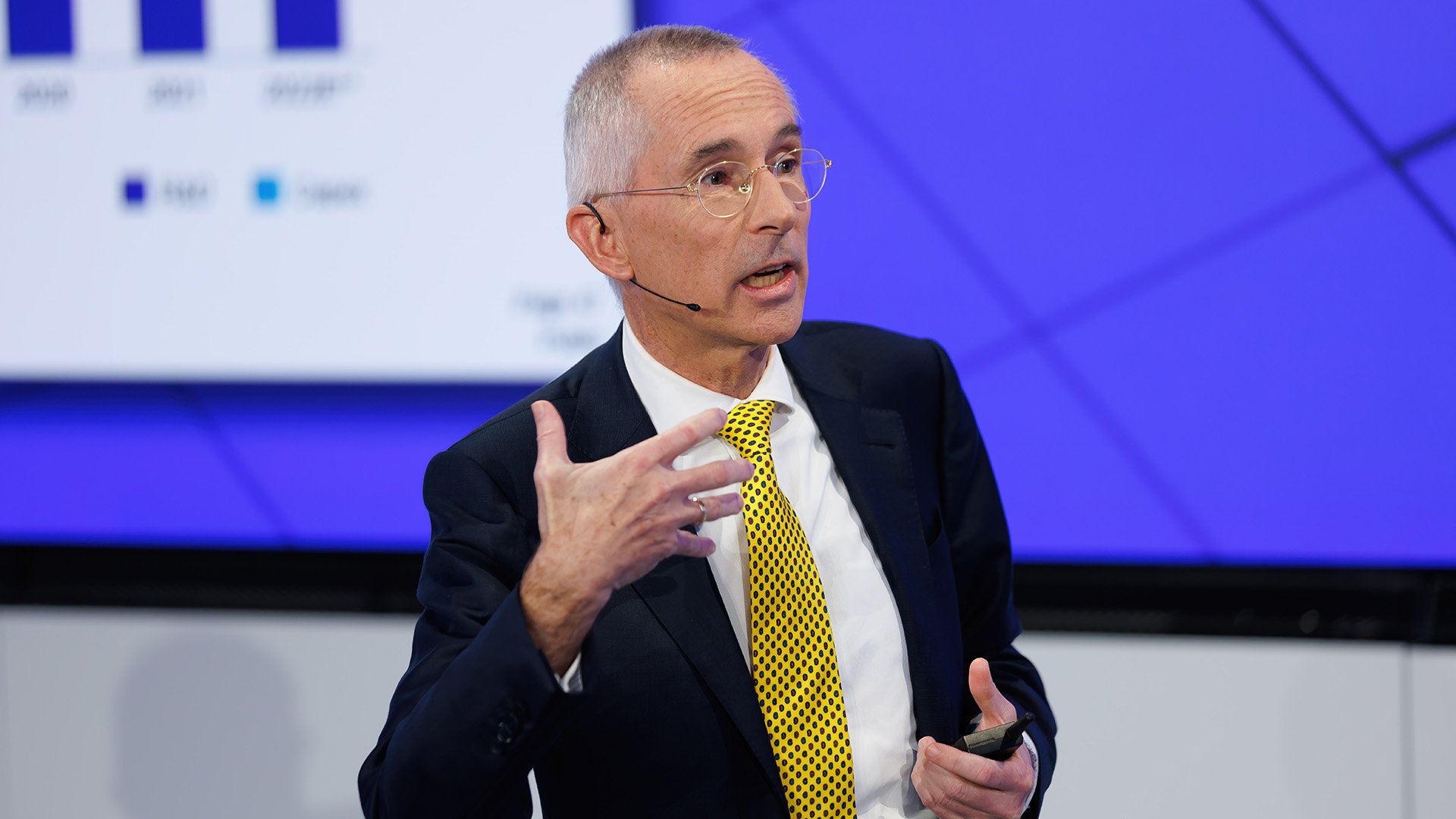 Man in a yellow tie gesturing while speaking on stage