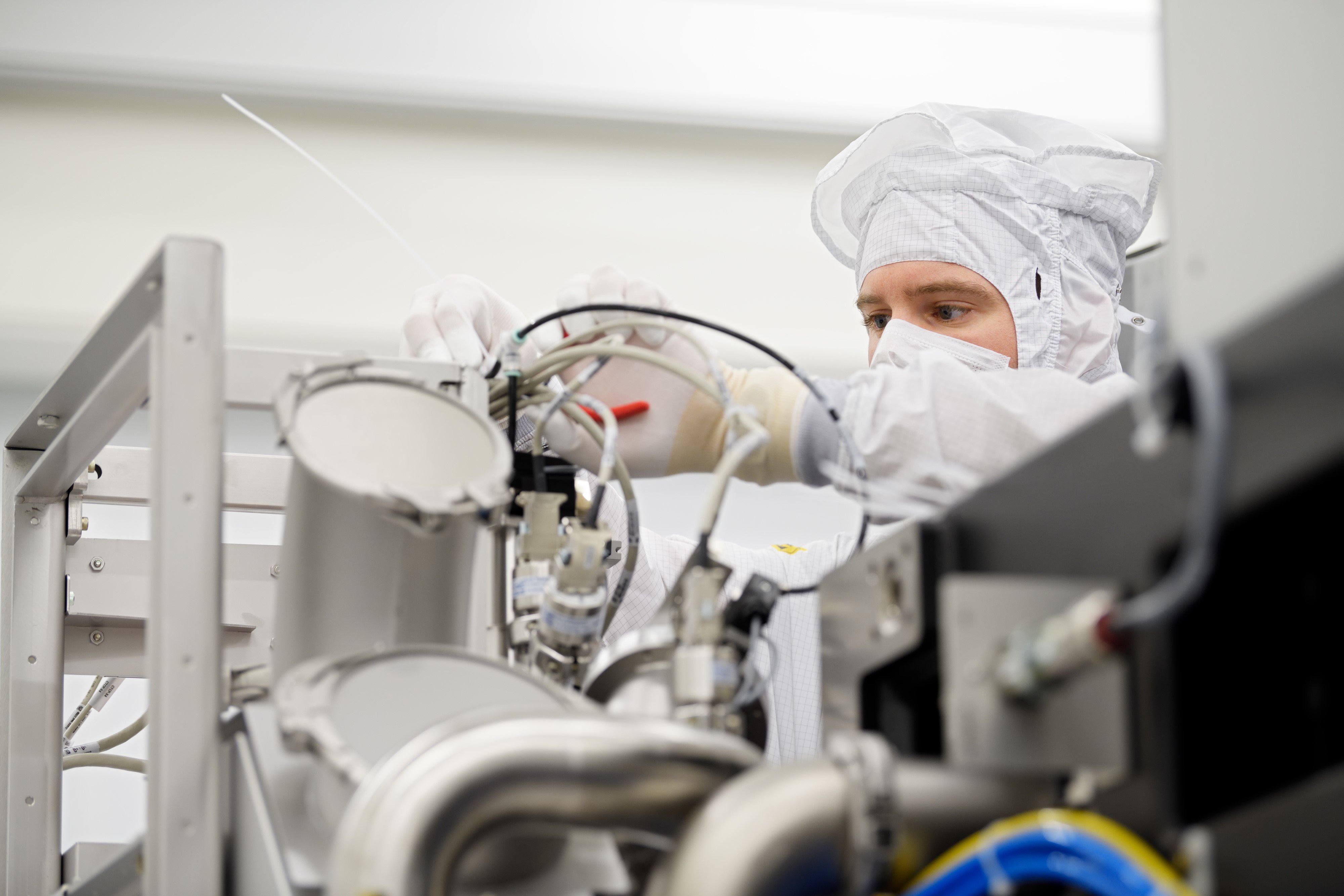 Een ASML medewerker draagt een cleanroom pak en werkt aan een geavanceerde machine. Een ASML medewerker draagt een cleanroom pak en werkt aan een geavanceerde machine.
