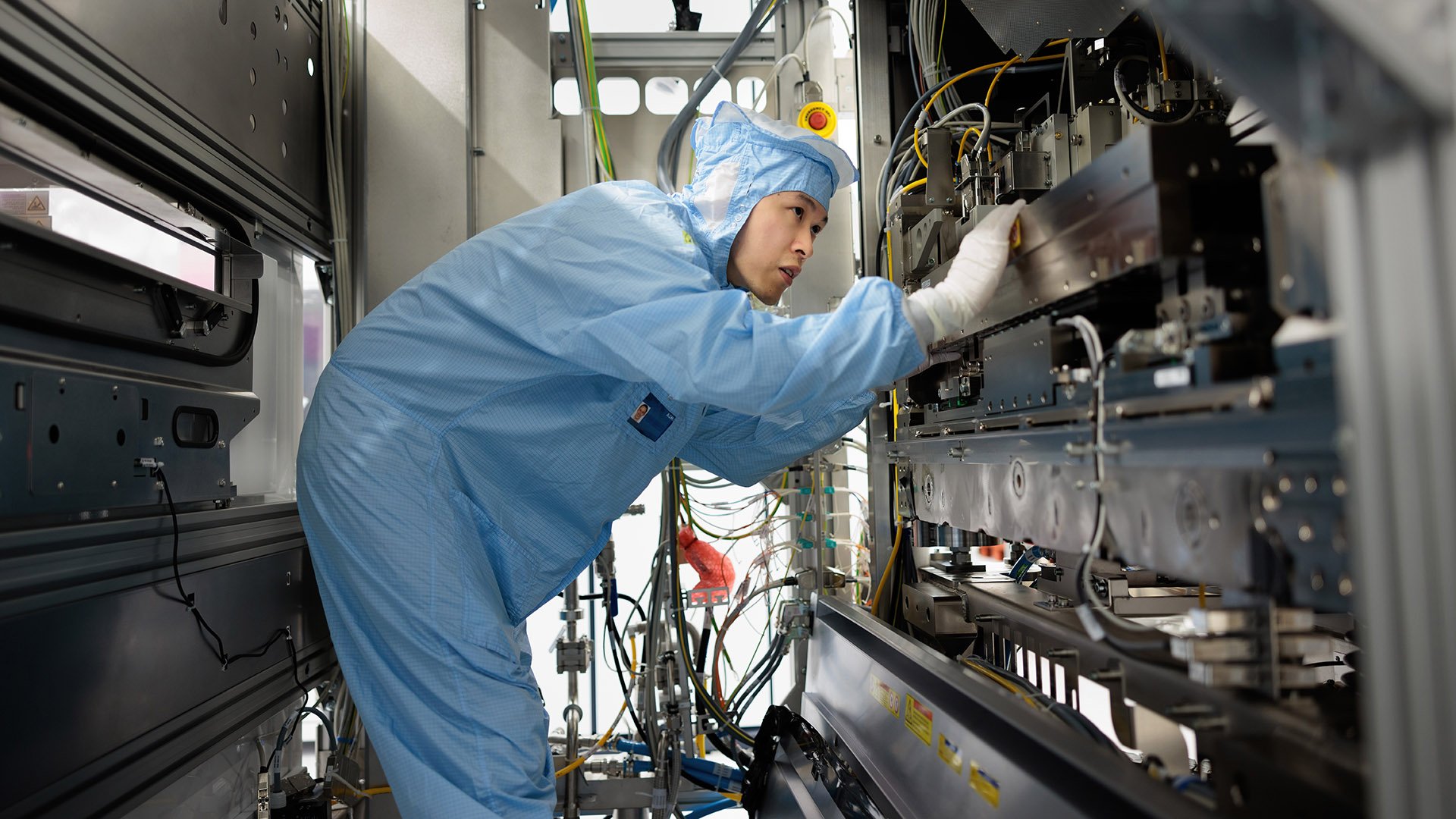 An ASML engineer in a cleanroom suit works on high-tech semiconductor manufacturing equipment. An ASML engineer in a cleanroom suit works on high-tech semiconductor manufacturing equipment.