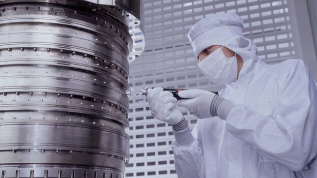 A person in a cleanroom suit makes an adjustment to the ZEISS projection optics system. A person in a cleanroom suit makes an adjustment to the ZEISS projection optics system.