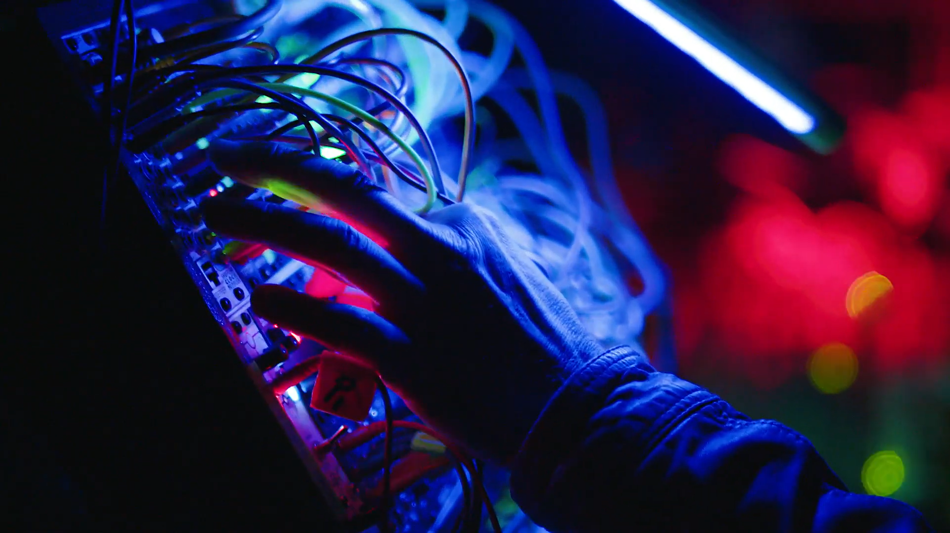 A hand on a glowing wired dashboard with multi-colored lights. A hand on a glowing wired dashboard with multi-colored lights.